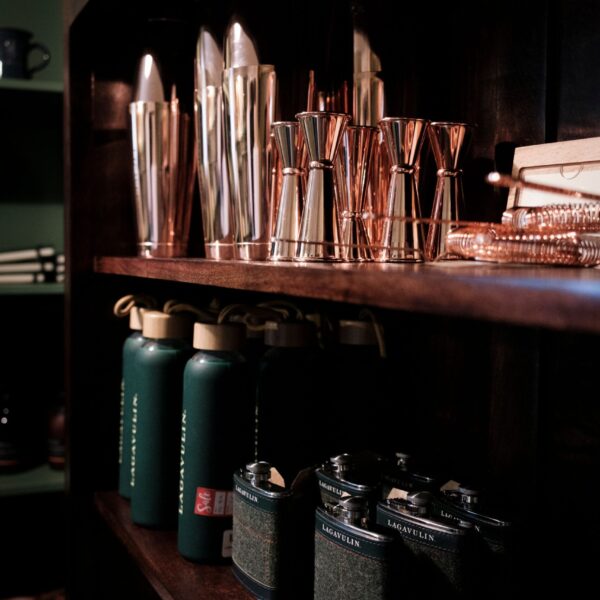 A collection of sleek barware and green bottles displayed on elegant wooden shelves in a softly lit room.