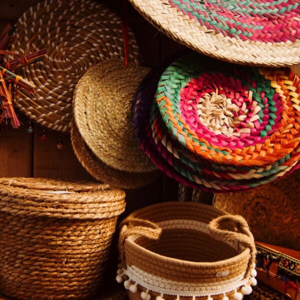 Colorful handmade woven baskets and hats displayed on a wooden wall, showcasing traditional craftsmanship.