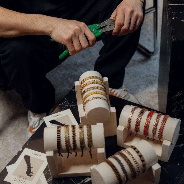 Close-up of artisan crafting bracelets with tools in a workshop. Detailed craftsmanship and design displayed.