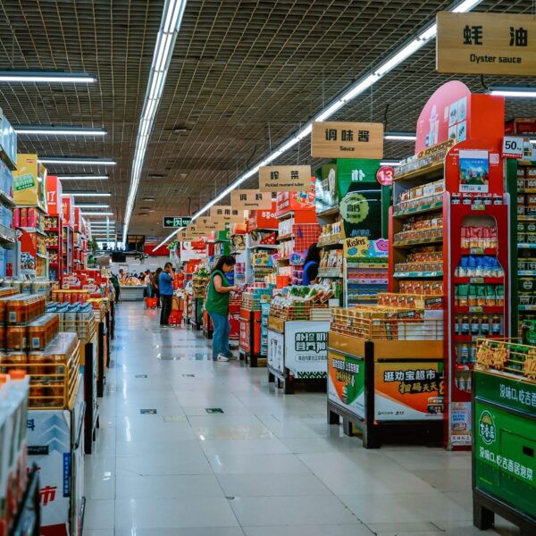 A vibrant supermarket aisle filled with diverse products and shoppers under bright lighting.